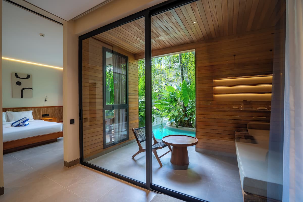 A modern room with a bed, a glass door leading to a pool, and a small table with chairs.