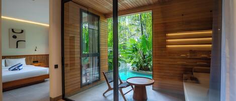 A modern room with a bed, a glass door leading to a pool, and a small table with chairs.