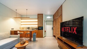 Un salon moderne comprenant un canapé, une table basse, un téléviseur, un coin cuisine et des meubles de rangement en bois.