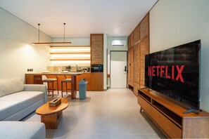 A modern living room with a sofa, coffee table, TV, kitchen area, and wooden cabinets. - Novo Ubud by Betterplace (Ubud)
