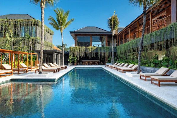 Una piscina con sillones de descanso y palmeras.