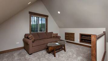 A loft bedroom with a sloped ceiling, a brown sofa, a glass coffee table, and wooden wall panels.