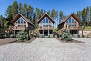 Eine dreigeschossige Lodge mit einem zentralen Eingang, hölzernen Balkonen und einer Schotterzufahrt.