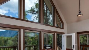 A dining area with a wooden table and chairs, large windows with a view of trees and mountains, and a hanging light fixture. - Family-Friendly Cabin Rental with Mountain Vistas near West Glacier, Montana (West Glacier)