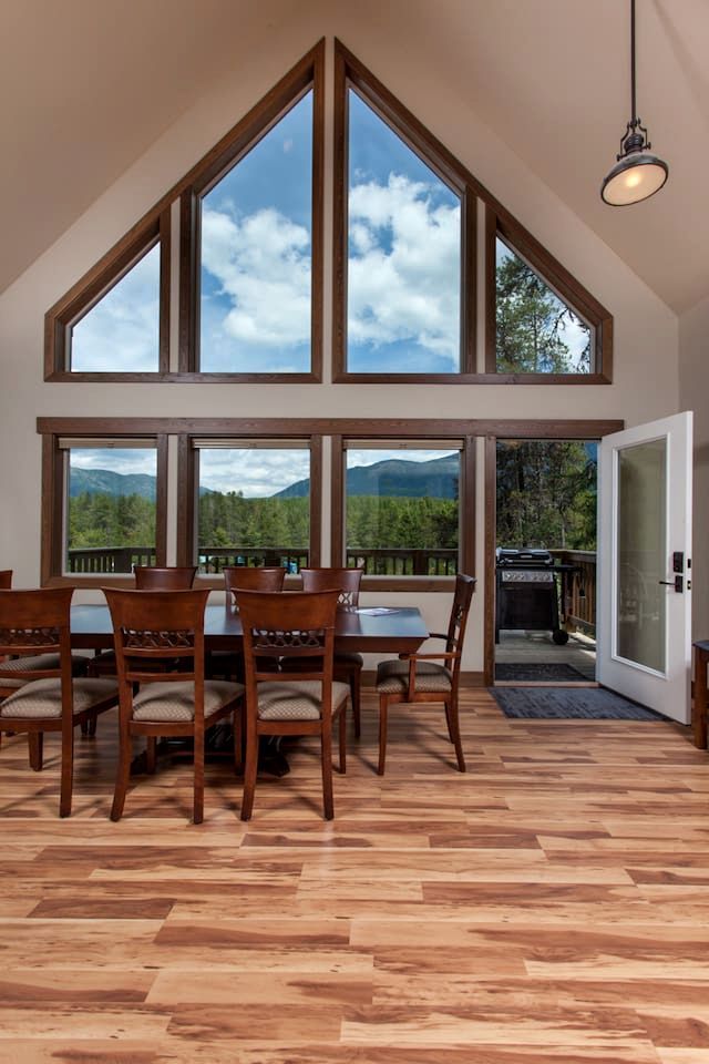 Un comedor con techo alto y ventanas amplias, suelo de madera y vista a las montañas.