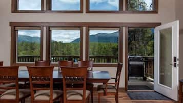 Un comedor con techo alto y ventanas amplias, suelo de madera y vista a las montañas.