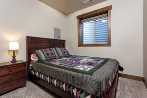 Ein Schlafzimmer mit einem Bett, einem Nachttisch, einer Lampe, einem Fenster mit Jalousien und einem Deckenventil.