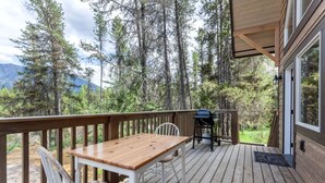 A wooden deck with a table and chairs, a grill, and a view of a forest and mountains. - Family-Friendly Cabin Rental with Mountain Vistas near West Glacier, Montana (West Glacier)