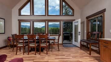 A dining area with a table and chairs, large windows with a mountain view, and a wooden floor.