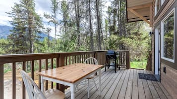 A wooden deck with a table and chairs, a grill, and a view of a forest and mountains.