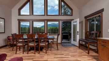 Un comedor con mesa y sillas, ventanas amplias con vista a la montaña y suelo de madera.