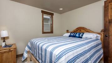 A bedroom with a bed, a nightstand, a lamp, a window, and a wooden door.