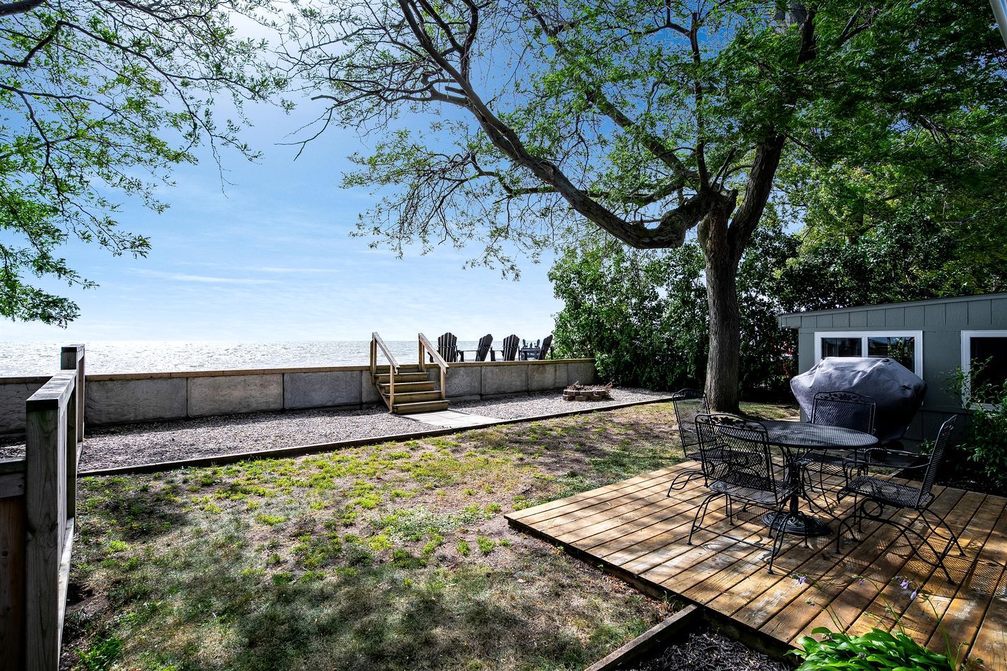 Une terrasse en bois, meublée pour l’extérieur, avec un barbecue et une vue sur la mer.