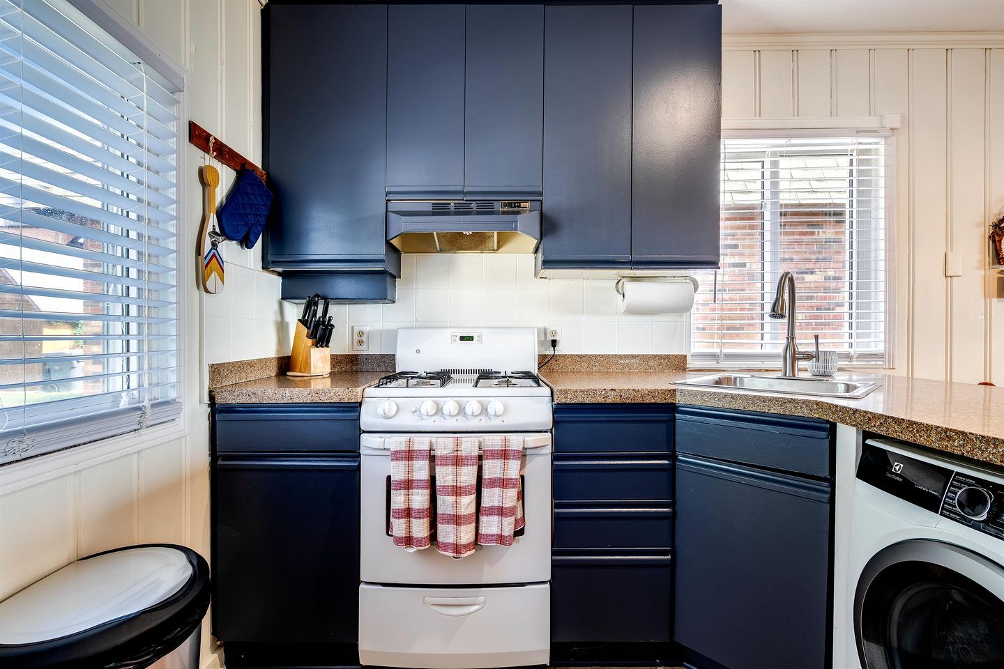 A compact kitchen with dark cabinets, a white stove, a washing machine, and a sink.