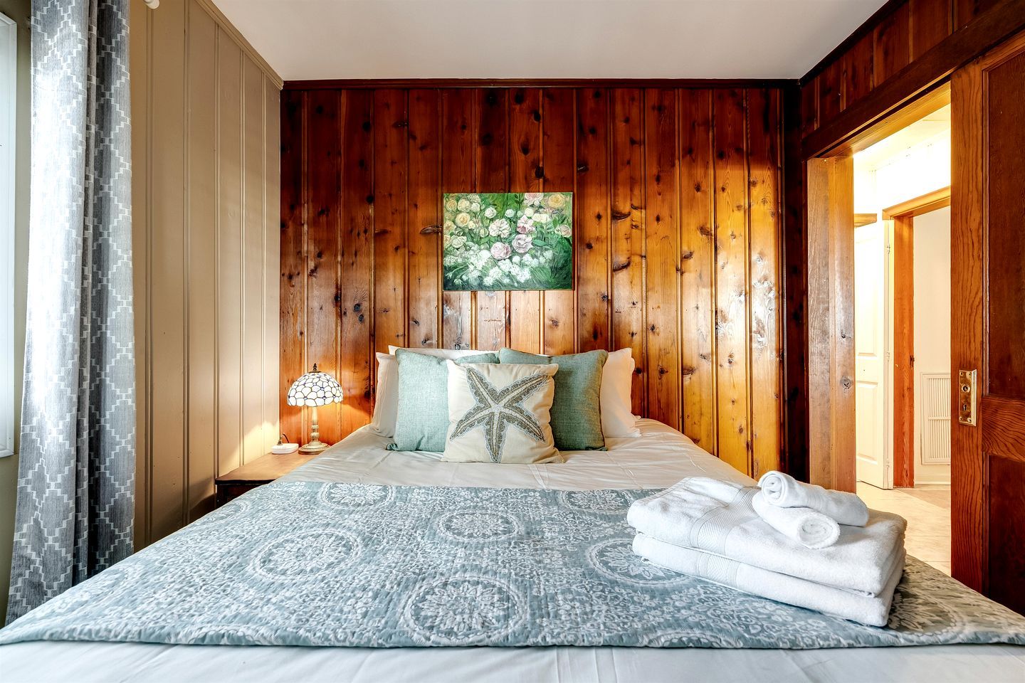 Ein Schlafzimmer mit Holzwandverkleidung, einem Bett, Kissen, einem Nachttisch, einer Lampe und einem Gemälde.