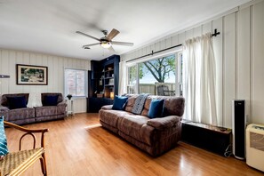 A living room with a brown leather sofa, a wicker chair, a ceiling fan, a bookshelf, and a window with curtains. - Cozy Rustic-Modern Cabin Escape with Lake Views & Fire Pit Nights in Ontario, Canada (Leamington)