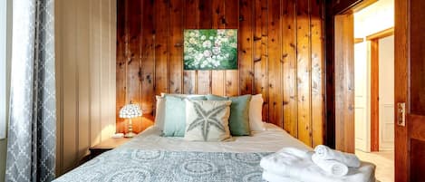 Ein Schlafzimmer mit Holzwandverkleidung, einem Bett, Kissen, einem Nachttisch, einer Lampe und einem Gemälde.