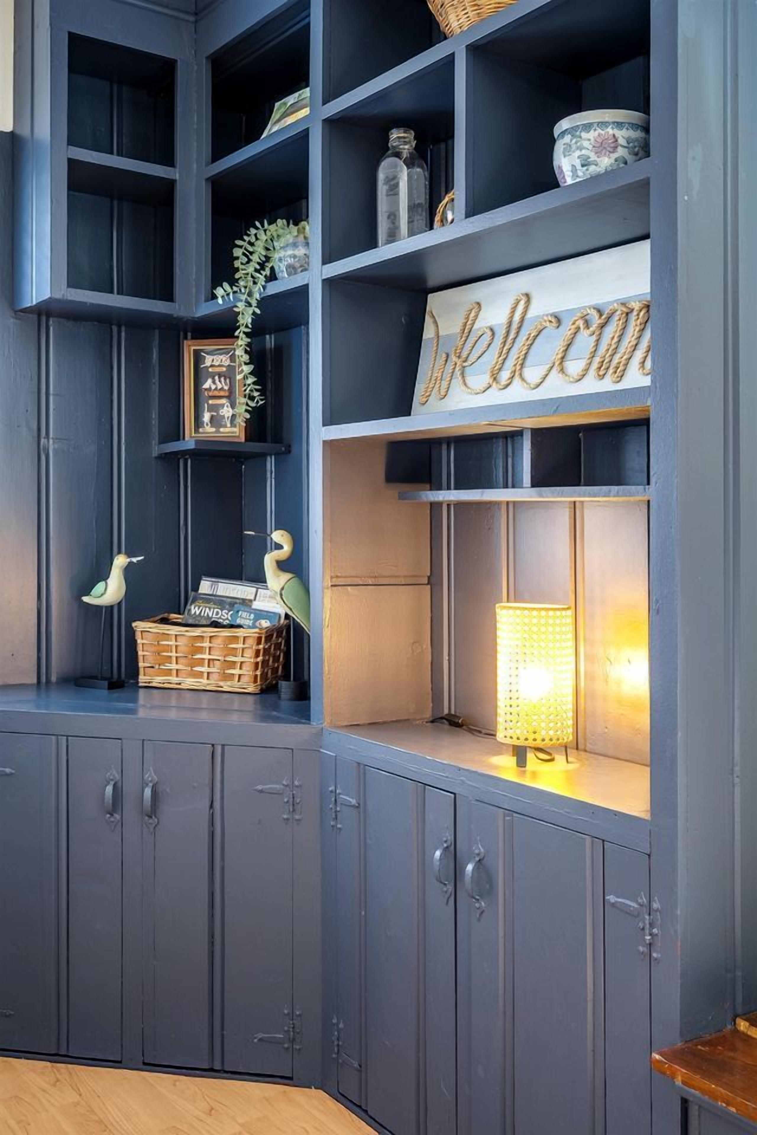 A dark blue room with shelves, a wicker basket, a lamp, and a welcome sign.