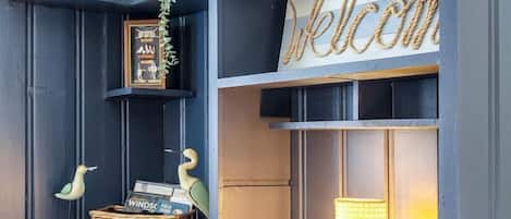A dark blue room with shelves, a wicker basket, a lamp, and a welcome sign.