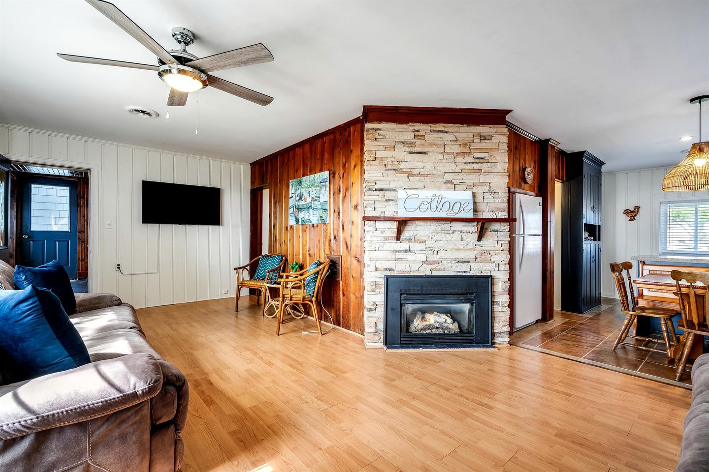 Un salon doté d’une cheminée, de murs en bois, d’un ventilateur de plafond et d’un coin repas.