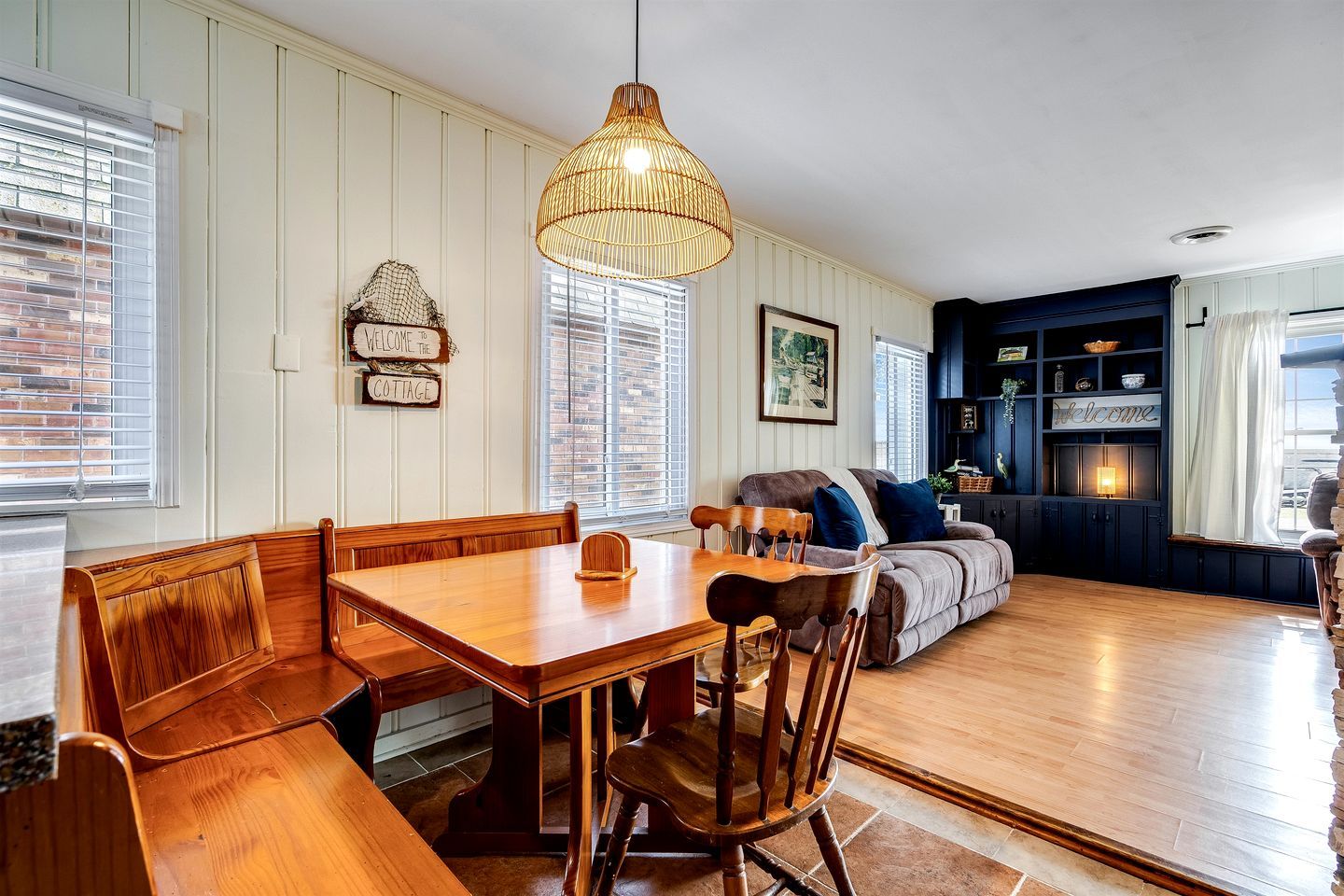A dining area with a wooden table and benches, a sofa, and a hanging light fixture.