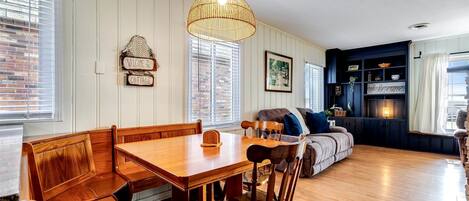 A dining area with a wooden table and benches, a sofa, and a hanging light fixture.