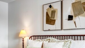 Ein ordentlich bezogenes Bett mit grüner Decke, weißen Kissen und einem Holz-Kopfteil. Eine Nachttischlampe steht auf einem Nachttisch neben dem Bett.