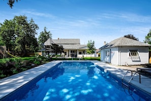 A residential swimming pool with a clear blue water surface, surrounded by a well-maintained lawn and trees. - Grand Victorian Farmhouse Escape with Pool, Hot Tub & Fire Pit Nights in Ontario, Canada (Leamington)