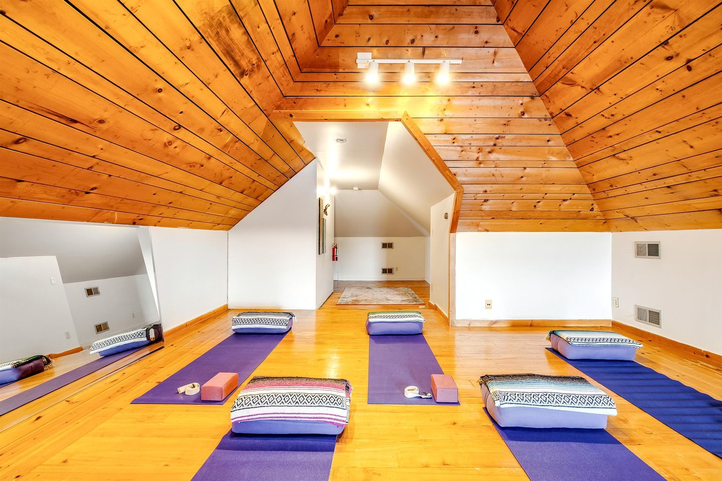 A yoga room with wooden ceilings and walls, multiple yoga mats, and a small rug.