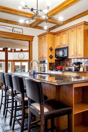 A kitchen with wooden cabinets, a central island with bar stools, a clock, and a chandelier. - Grand Victorian Farmhouse Escape with Pool, Hot Tub & Fire Pit Nights in Ontario, Canada (Leamington)
