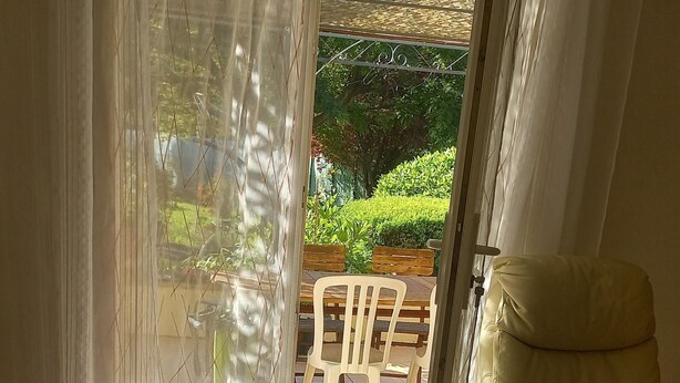 A room with a bed, a white sofa, a patterned rug, and a view of an outdoor patio with chairs and greenery. - Charming downstairs villa (Forcalquier)