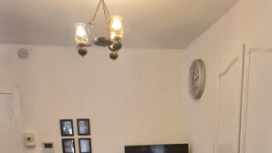 A dining area with a long table, chairs, a chandelier, a television, and a clock on the wall. - Charming downstairs villa (Forcalquier)
