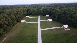 Uma propriedade rural com quatro cabanas brancas, um caminho pavimentado central e floresta densa ao redor.