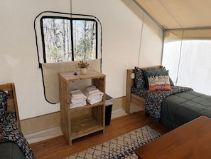 Interior acollidor d'una caravana amb una estant de fusta plena de tovalloles, una finestra que dona a vistes d'arbres i un llit amb llençols estampats i un coixí amb una frase motivacional.
