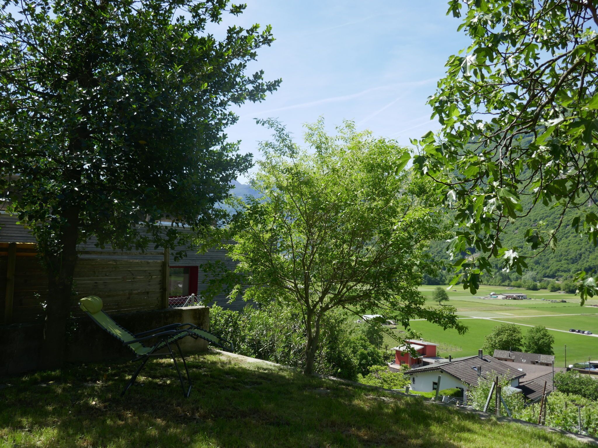 Een uitzicht op een huis met een boom op de voorgrond, een gazon en een weids uitzicht op een veld en bergen.