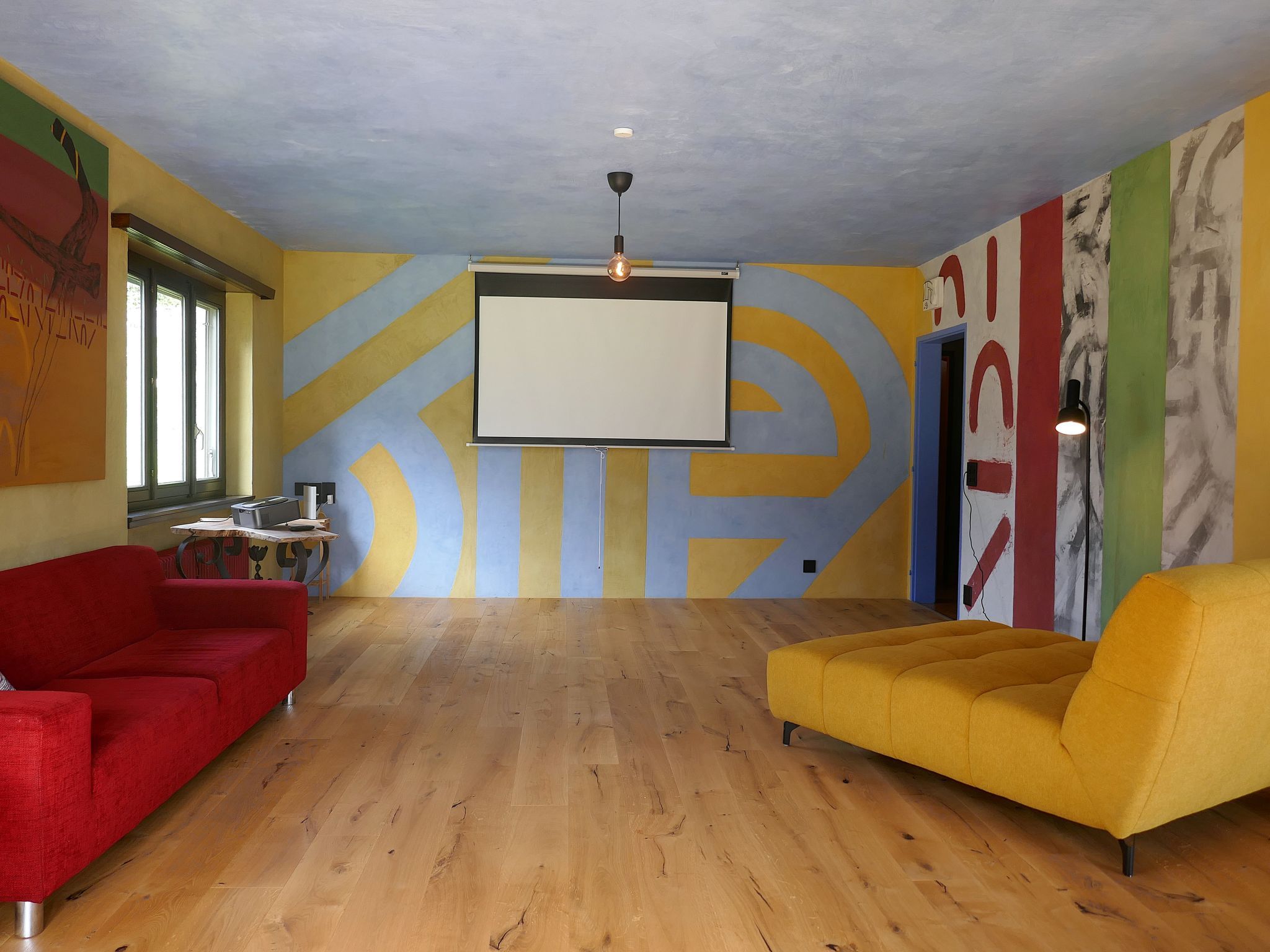 Ein geräumiges Zimmer mit einem großen Bildschirm, zwei Sofas und Holzboden.