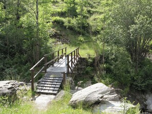 Eine Holzbrücke mit Geländern über einen steinigen Weg in einem bewaldeten Gebiet.