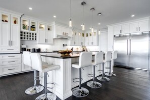 Une cuisine moderne avec des meubles blancs, un îlot central doté de tabourets, des appareils en acier inoxydable et un éclairage suspendu.