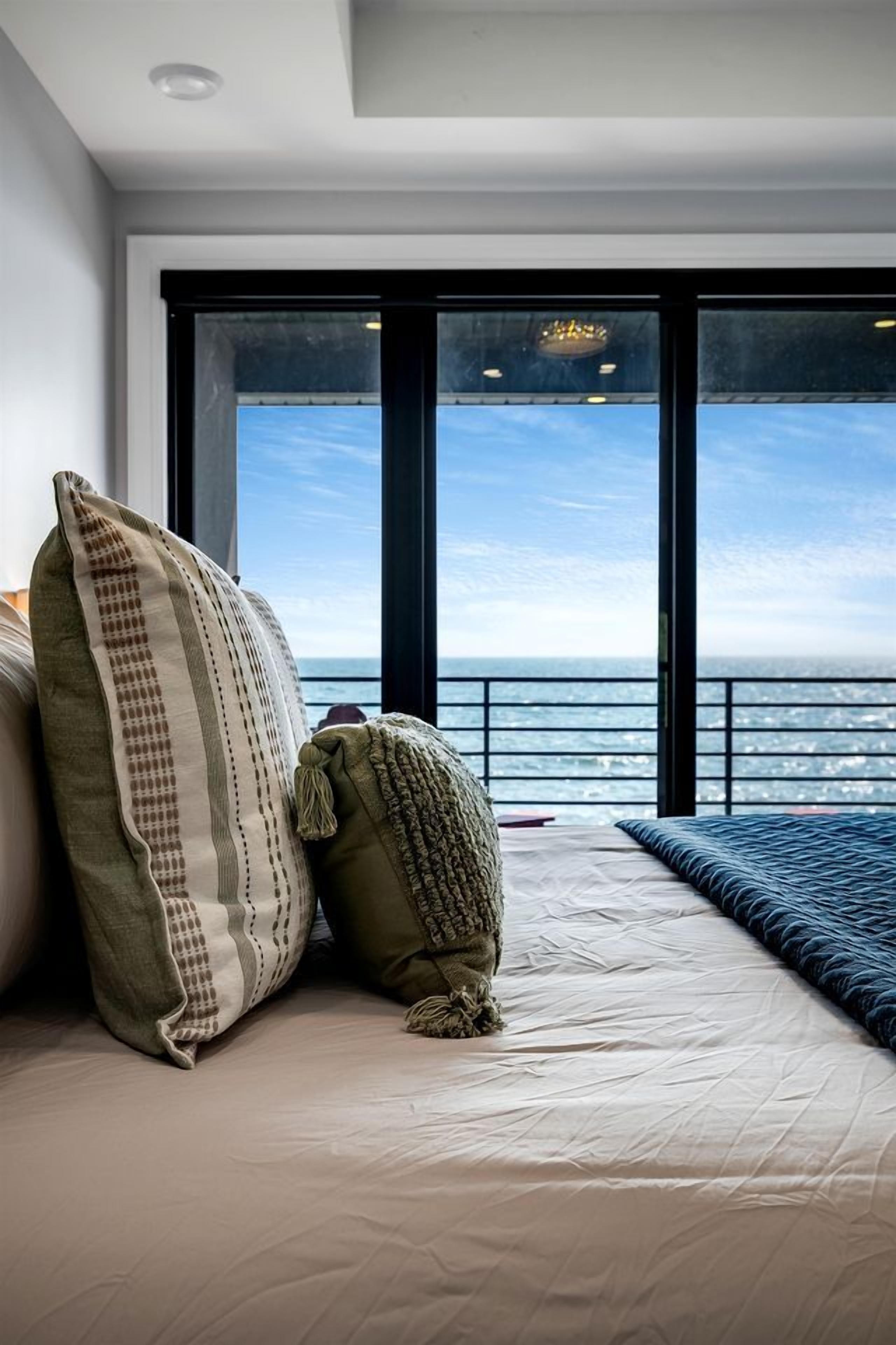 A bedroom with a large window, a bed, and a view of the sea.