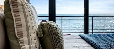 A bedroom with a large window, a bed, and a view of the sea.