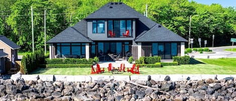 Una casa moderna de dos pisos con un amplio porche delantero, un muro de contención de piedra y vistas al agua.