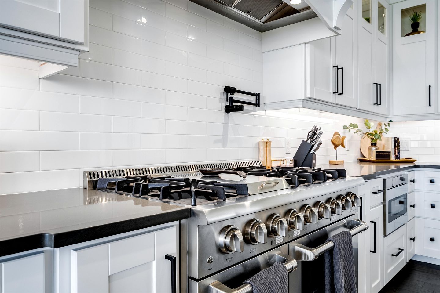 A modern kitchen with white cabinetry, a stainless steel stove, and a black countertop.
