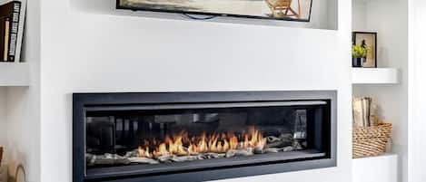 Ein modernes Wohnzimmer mit einem Flachbildfernseher über einem Kamin, einer Couch und einem flauschigen Teppich.