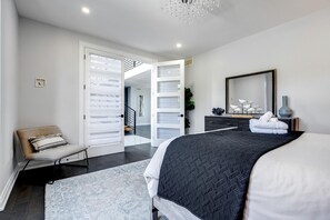 A bedroom with a bed, a chair, a dresser, a mirror, and a staircase leading to an upper floor.