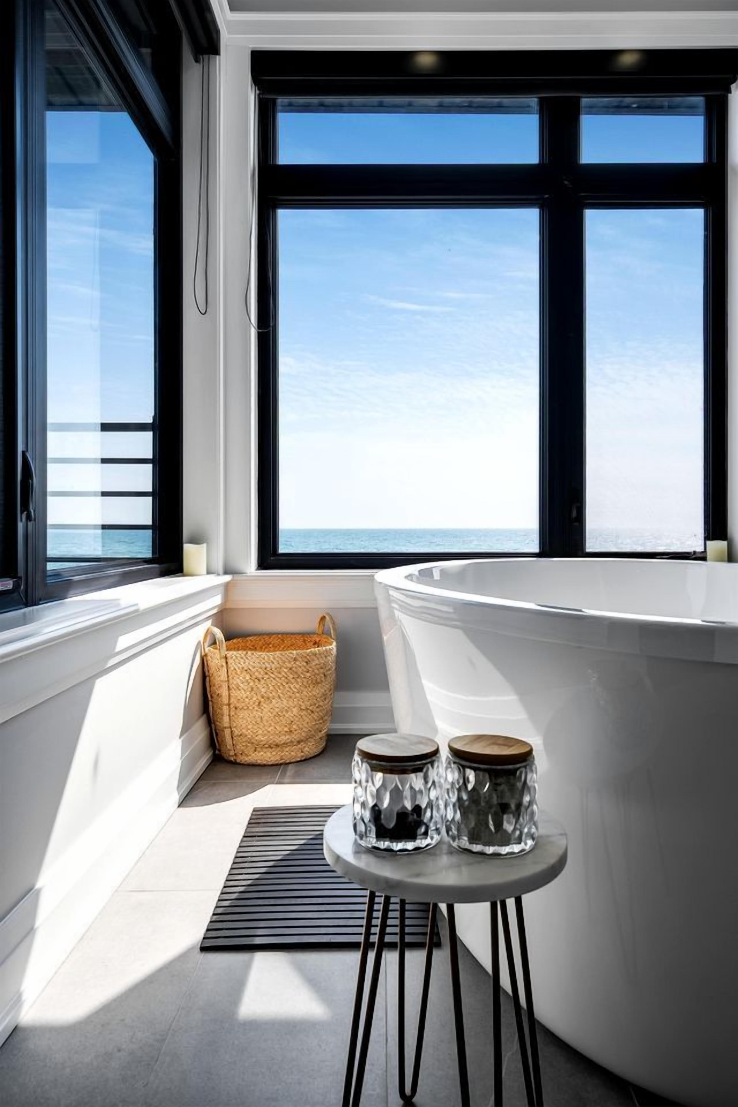 Une salle de bain moderne avec une baignoire, un panier en osier et deux bocaux en verre posés sur une petite table.