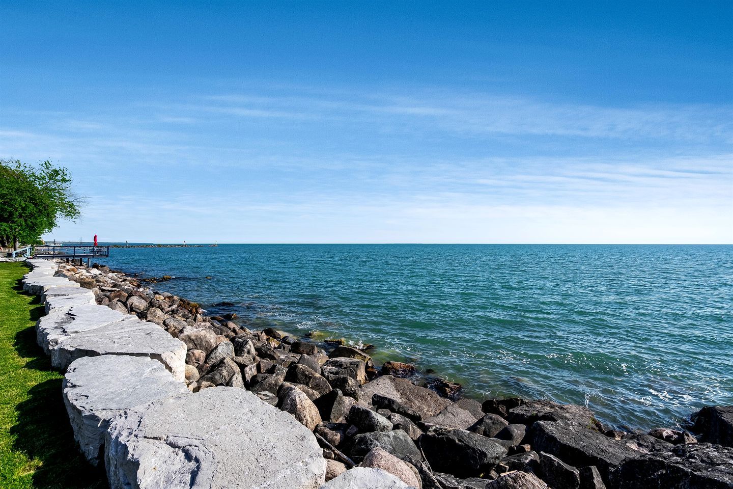 A coastal walkway with a stone barrier, a grassy area, and a clear blue sky.