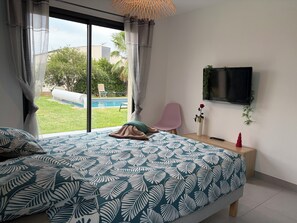 A bedroom with a large bed, a TV mounted on the wall, and a view of a swimming pool outside. - Chill House (Narbonne)