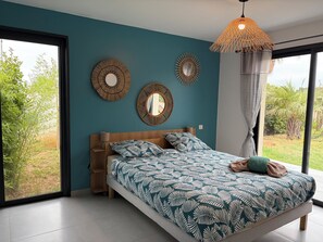 A bedroom with a bed, two wall mirrors, a hanging light fixture, and a view of greenery outside. - Chill House (Narbonne)