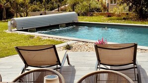 Un área junto a la piscina con dos sillas de descanso, una mesa con lámpara y vista a la piscina.
