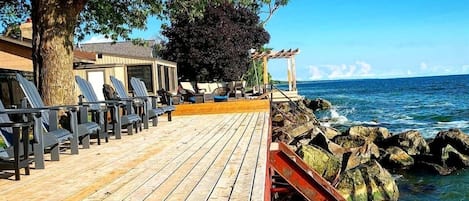 A wooden deck with lounge chairs, a pergola, and a view of the ocean.